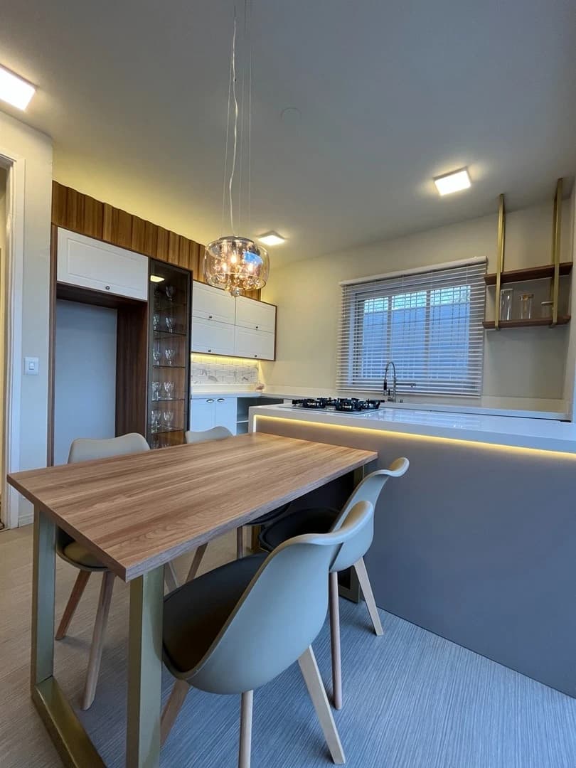 Cozinha Moderna com Detalhes Elegantes: Ambiente em estilo moderno, com mesa de madeira clara e cadeiras em tom neutro. Materiais sofisticados e iluminação suave destacam a funcionalidade.