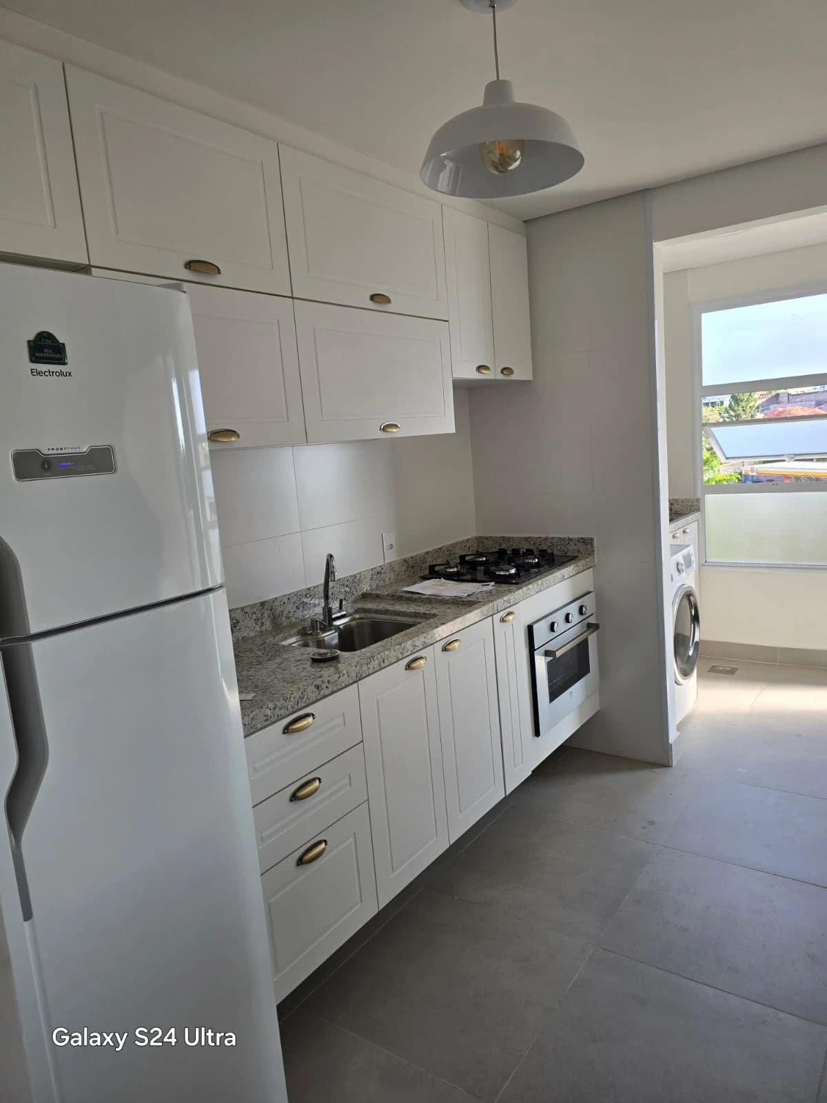 Cozinha Moderna com Toques Elegantes: Ambiente clean em tons claros, com armários brancos e detalhes em dourado. Materiais como granito e piso em porcelanato garantem funcionalidade e sofisticação.