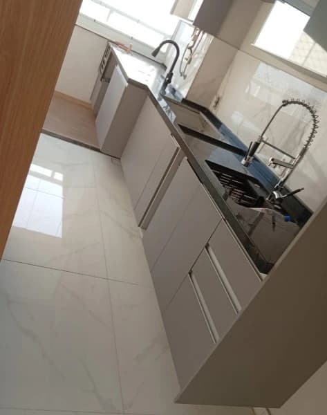 Cozinha Moderna com Acabamentos Elegantes: Ambiente funcional com armários em MDF, bancada de granito preto e piso em porcelanato. Cores neutras e iluminação natural destacam a modernidade do espaço.